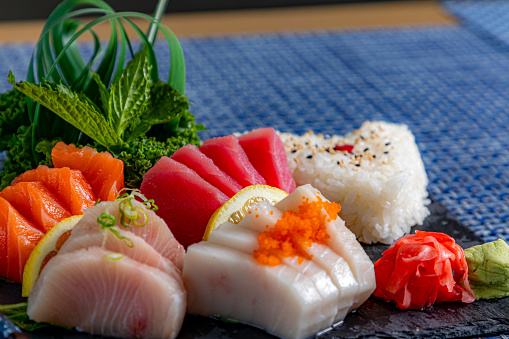 A woman hand wields chopsticks to delicately place fresh salmon sashimi on a plate in a Japanese restaurant, capturing the art of dining.