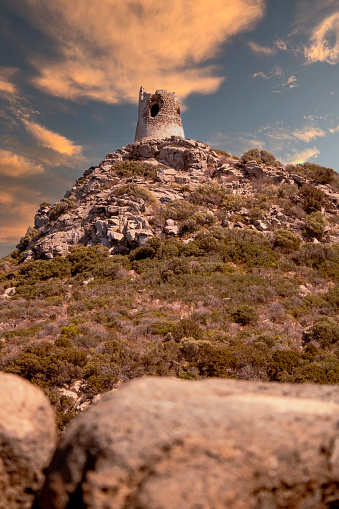 Tramonto sulla torre diroccata di Porto Giunco in Sardegna a villasimius. La scogliera cade a picco sul mare. Intirno c’è tutta la macchia mediterranea con alberi e arbusti. Il tramonto colora il cielo di rosso