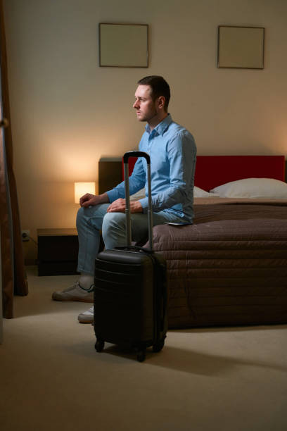 istock Man looking out window sitting on bed in hotel room 1509720892