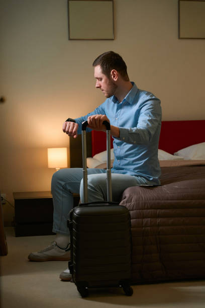 istock Man looking at clock sitting on bed in hotel room 1509720895