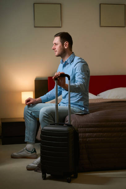 istock Handsome guy looking in window sitting on bed in hotel room 1509720902