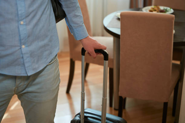 istock Young man holding handle of suitcase standing in hotel room 1509721426