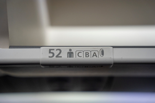 Close up on  52 A, B, C  row and seat identifier on an overhead bin of a commercial passenger aircraft.