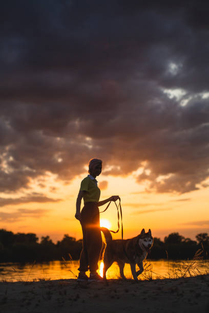istock Woman with dog silhouette at sunset sky background. River bank 1509779055