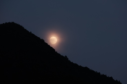 A majestic full moon illuminated against a backdrop of a mountainous landscape
