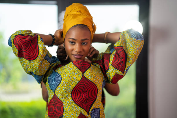 Beautiful young black woman putting on a headscarf while her friend is helping her from behind.