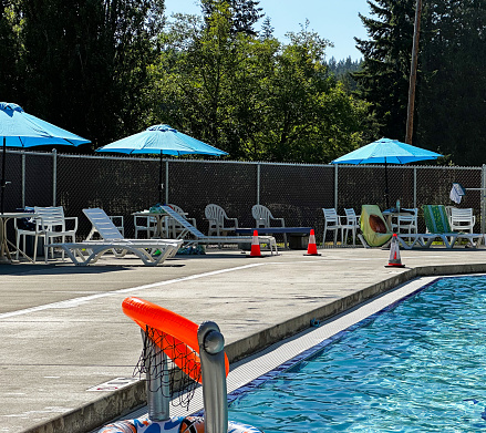 Shade umbrellas and chairs with towels sit next to a sparkling blue outdoor swimming pool.