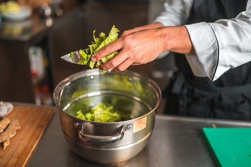 Male hands display exceptional knife skills as they efficiently cut a lettuce. He is putting the lettuce on a large metal bowl.