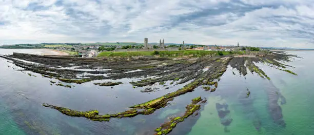 Drone panorama view of St. Andrews, Fife Scotland with rocky coastline and village at low tide.