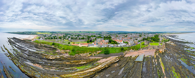 Drone panorama view of St. Andrews, Fife Scotland with rocky coastline and village at low tide.