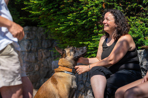 The dog, a Belgian shepherd, listens attentively and devotedly to its owner during a conversation with friends, Real people, sunny day