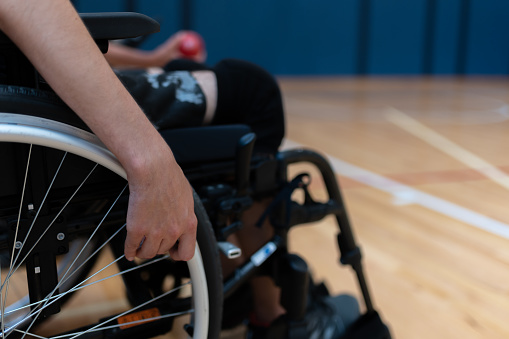 The hand of a disabled person in a wheelchair holding the wheel of the wheelchair and pushing it off.