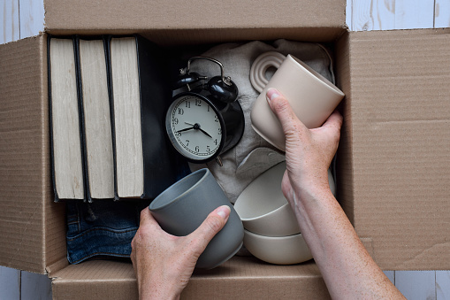 Person's hands placing used personal belongings items into cardboard box, donations, thrifting or moving concept