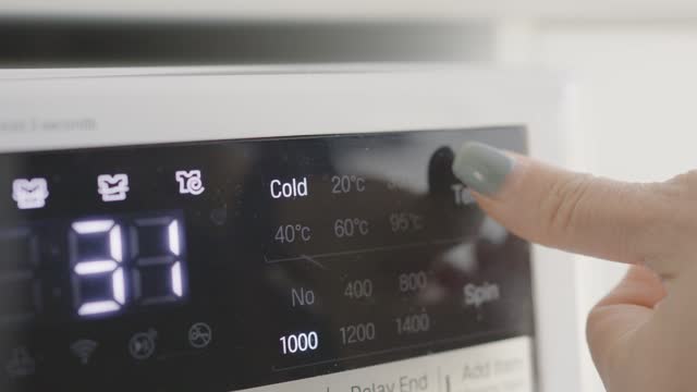 Woman hands turning washing machine dial to cold washing mode, energy saving concept