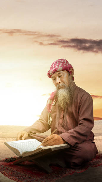 Muslim man with a beard wearing keffiyeh with agal sitting and reading the Quran on the prayer rug Muslim man with a beard wearing keffiyeh with agal sitting and reading the Quran on the prayer rug with the sunset scene background middle eastern ethnicity mature adult book reading stock pictures, royalty-free photos & images