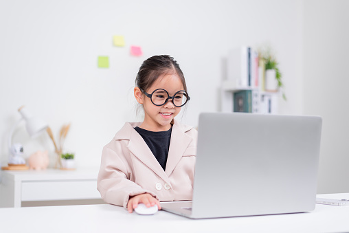 Little business lady Asia. Cute little girl in glasses and formalwear sitting at the table and using laptop