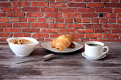 Continental breakfast, a plate of oatmeal with raisins and nuts, fresh croissants and a cup of hot black coffee on a wooden table.
