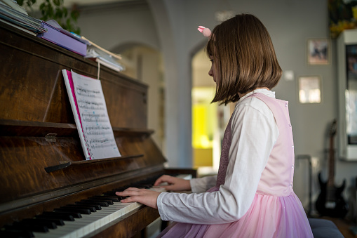 Side view of girl playing piano. Cute female child is practicing on musical instrument. She is at home.