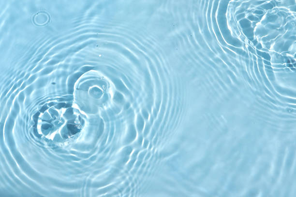 istock Drops falling into the water leaving circles on the water. blurred transparent blue colored clear calm water surface texture with splash and bubbles. Texture of water surface reflections. 1510395236