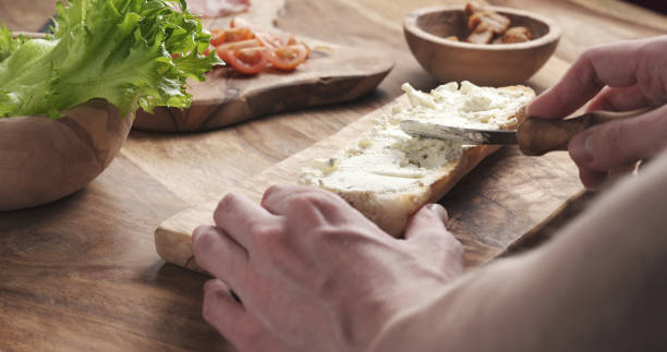 man spread cream cheese with herbs over baguette in slow motion