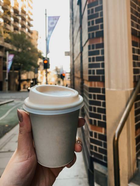 istock Hand holding grey paper cup with white lid on the sideway behind the red light beside the brick wall cafe 1510458242