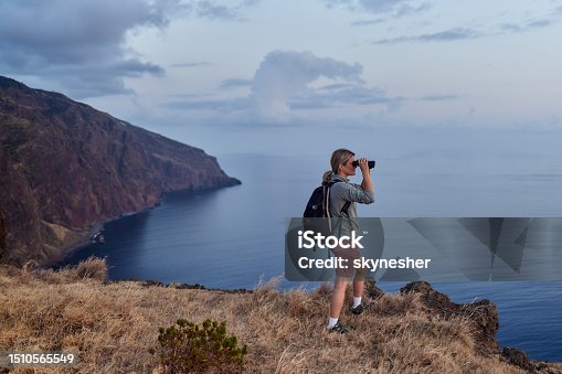 istock Carefree female backpacker looking through binoculars from a hill. 1510565549