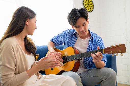 Couple of man and woman playing guitar together at home on weekend, Happy people enjoying and relaxing at home, People lifestyle, Romantic couple with good relationship. High quality photo