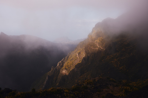 View of the sunlight lightening part of the mountain during foggy day in Madeira, Portugal.