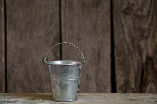 gray metal empty bucket on wooden background closeup