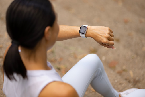 Close up of a female athlete checking her daily progress on smartwatch while having a break in nature.