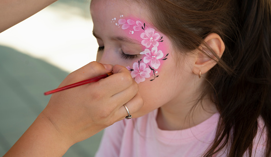 The artist makes a drawing on the girl's face with a face painting.