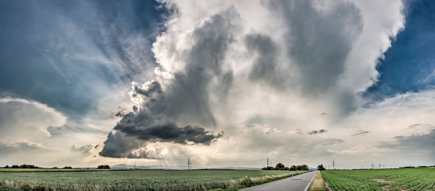 A thundercloud in a dramatic cloudy sky passes over agricultural land with its wispy clouds