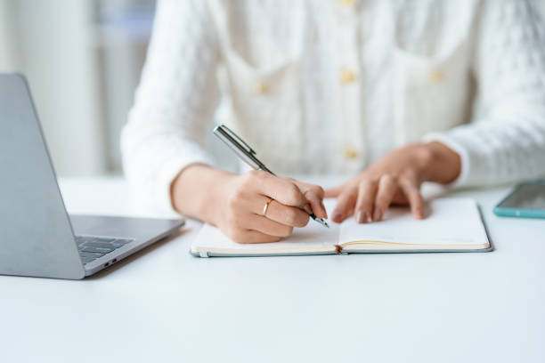 istock Close-up of a woman taking notes on notebook with laptop in office. 1510679010