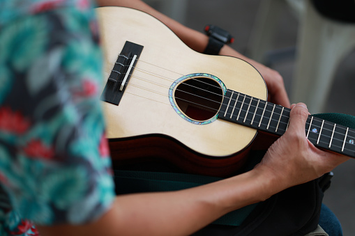 From a zenithal perspective, an unrecognizable man is seen holding his ukulele while waiting for his turn to perform.