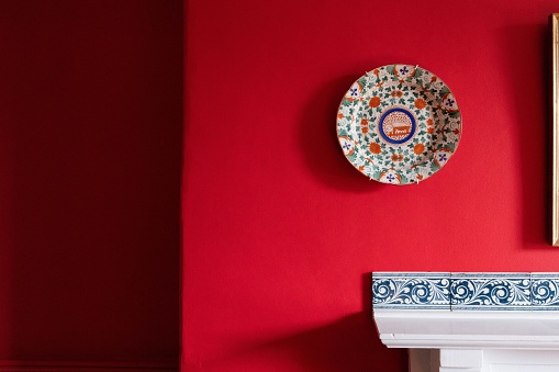 A decorative painting on a plate on a deep red wall in a cozy room