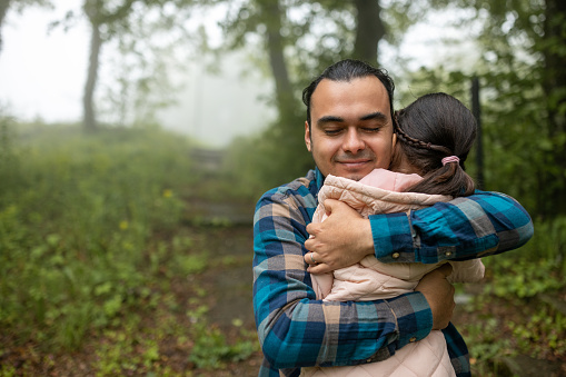 Mid adult Hispanic man hugging his daughter in a forest