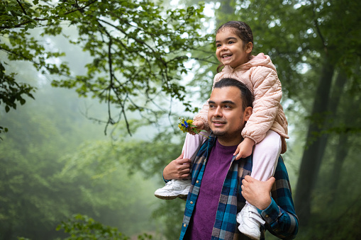 Mid adult Hispanic man carrying his daughter on his shoulders while walking in a forest