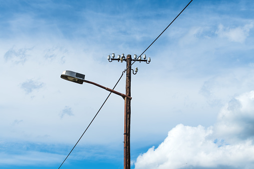 Old street light lamp and electricity pole against blue sky