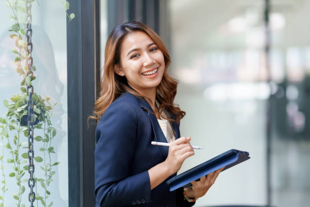 Attractive smiling Asian businesswoman standing holding tablet working and recording work details in office. Attractive smiling Asian businesswoman standing holding tablet working and recording work details in office. chief of staff stock pictures, royalty-free photos & images