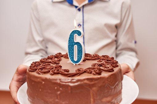 A boy is holding a festive cake with a candle in the form of the number 6. The concept of a birthday celebration.