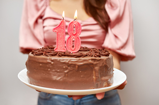 The girl is holding a festive cake with a candle in the form of the number 18. The concept of a birthday celebration.