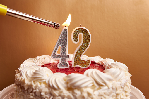 A candle in the form of the number 42, stuck in a festive cake, is lit. Celebrating a birthday or a landmark event. The climax of the celebration.