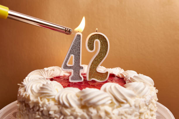 A candle in the form of the number 42, stuck in a festive cake, is lit. Celebrating a birthday or a landmark event. The climax of the celebration. A candle in the form of the number 42, stuck in a festive cake, is lit. Celebrating a birthday or a landmark event. The climax of the celebration. number 42 stock pictures, royalty-free photos & images