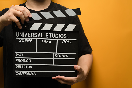 Man holding black clapperboard on yellow background. Video production, film, cinema industry concept.