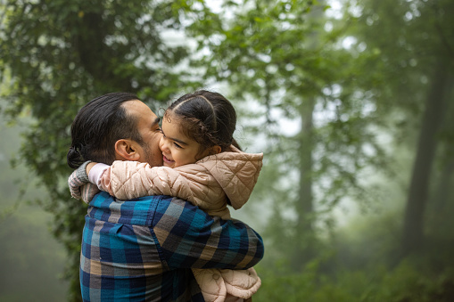 Mid adult Hispanic man and his daughter embracing in the forest