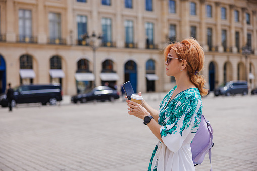 Elegant woman standing on a town square in Paris and using her mobile phone, travel lifestyle