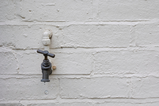 Old metal water pipe and faucet near an exterior wall. Close up shot, no people.