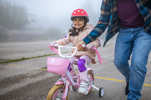 Little Hispanic girl riding a bicycle with the help of her father