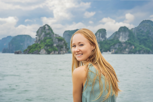Attractive woman in a dress is traveling by boat in Halong Bay. Vietnam. Travel to Asia, happiness emotion, summer holiday concept. Picturesque sea landscape. Ha Long Bay, Vietnam.