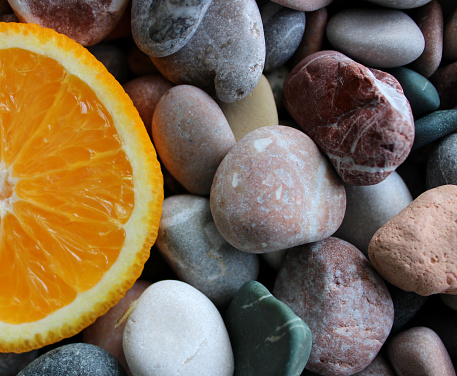 Fragment Of Orange Fruit Cut In A Half On A Round Stones At A Side Of Image